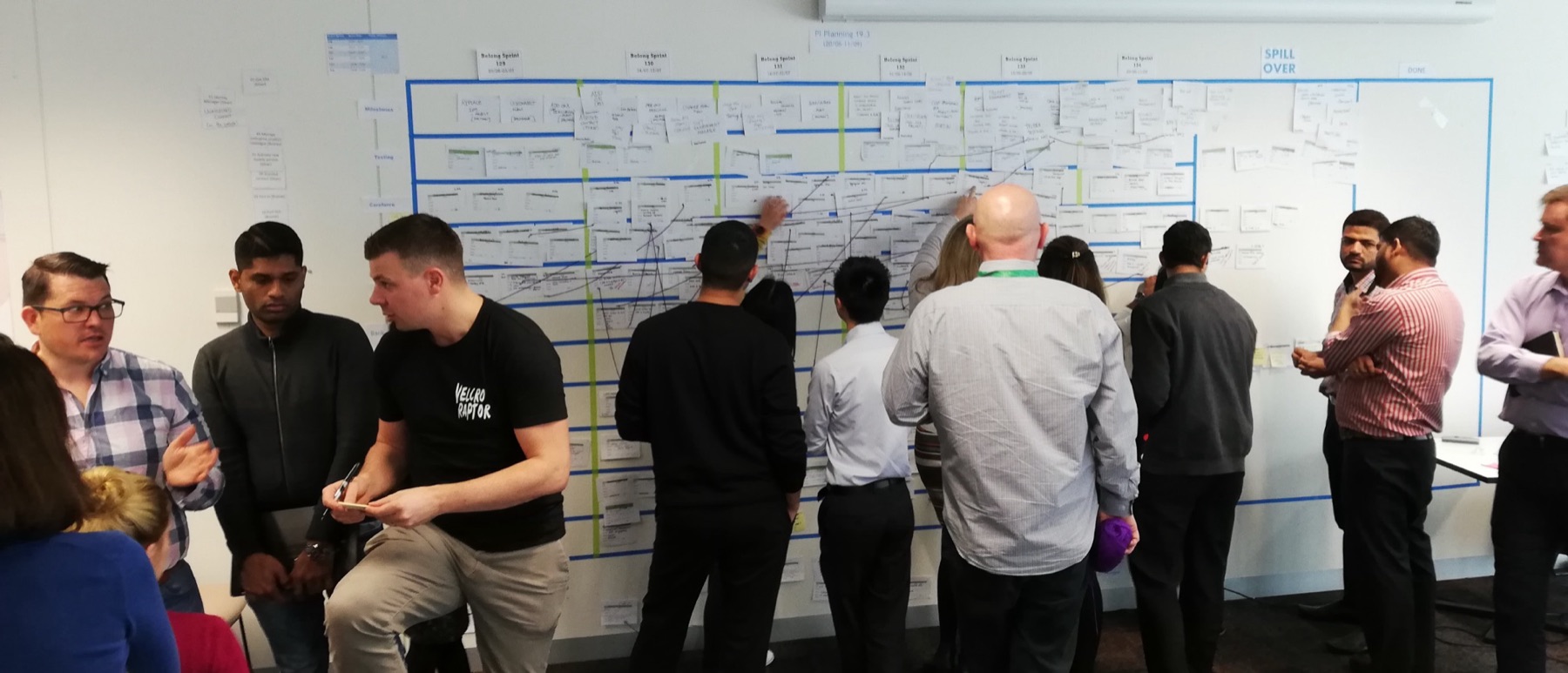 Wide view of a workshop room, participants working across a full-wall printed chart